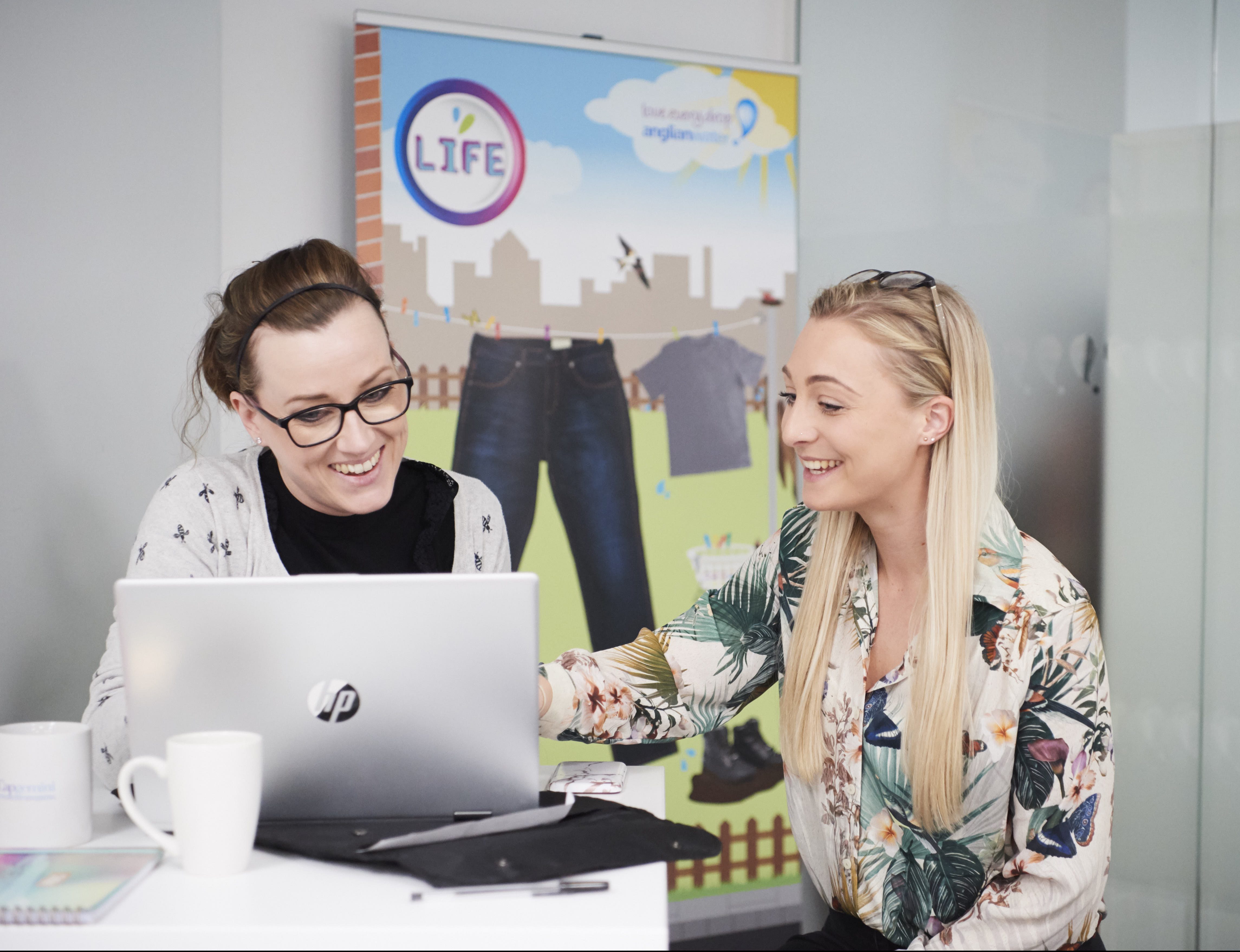 Two females sitting at table in office environment looking at laptop