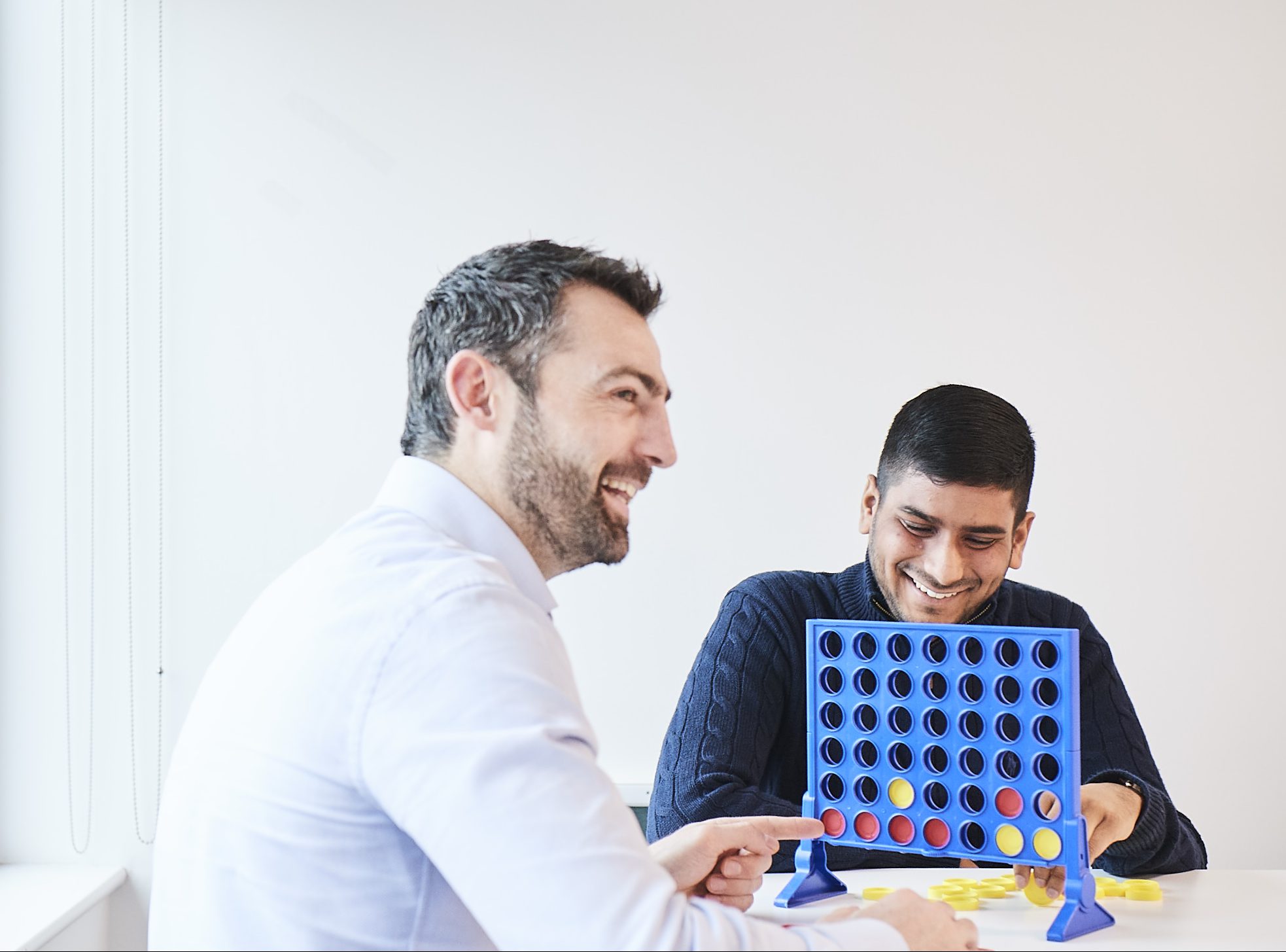 Close up shot of two male colleagues sitting at a table playing connect 4