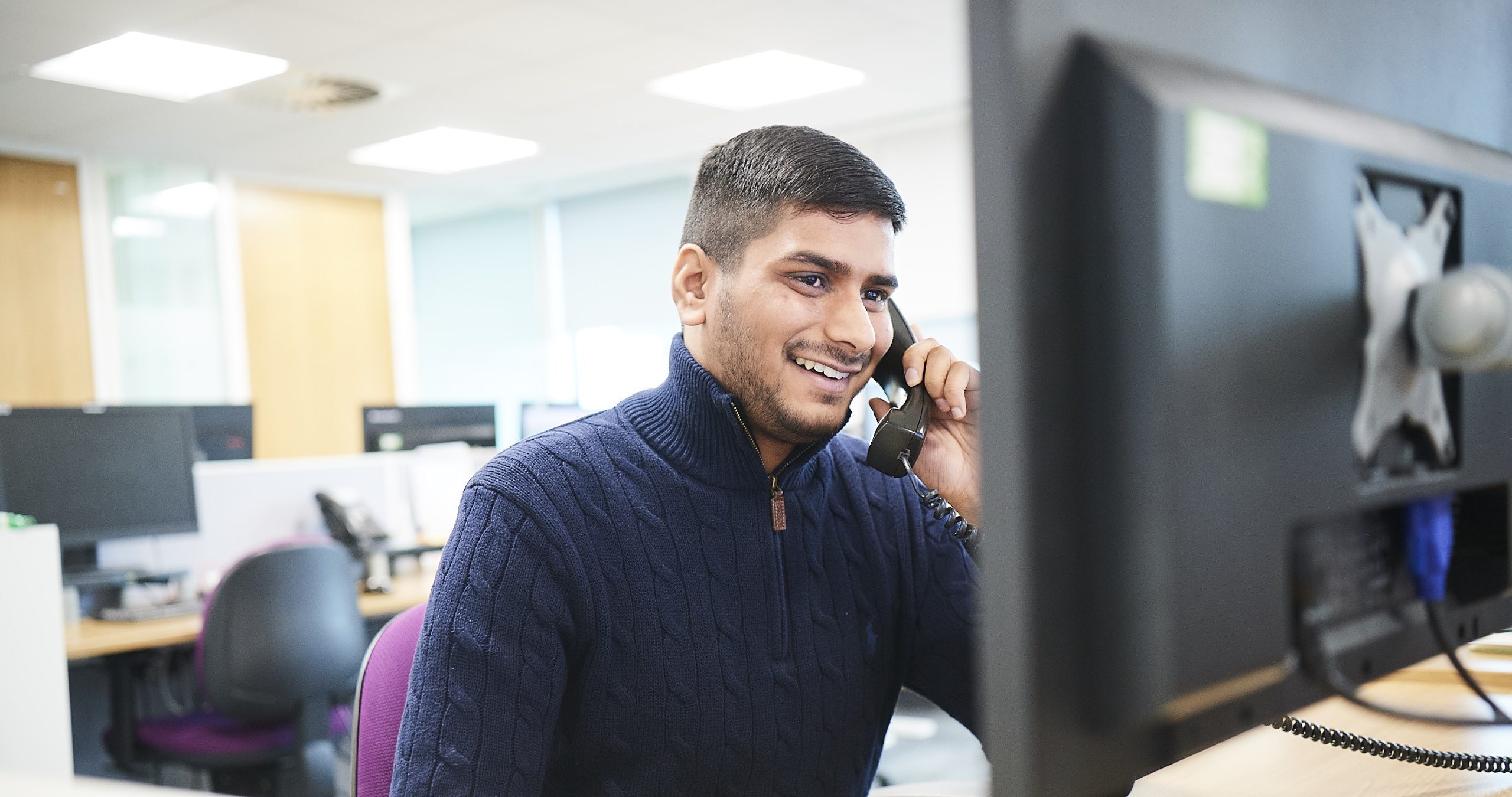 Male at desk on phone looking at computer screen