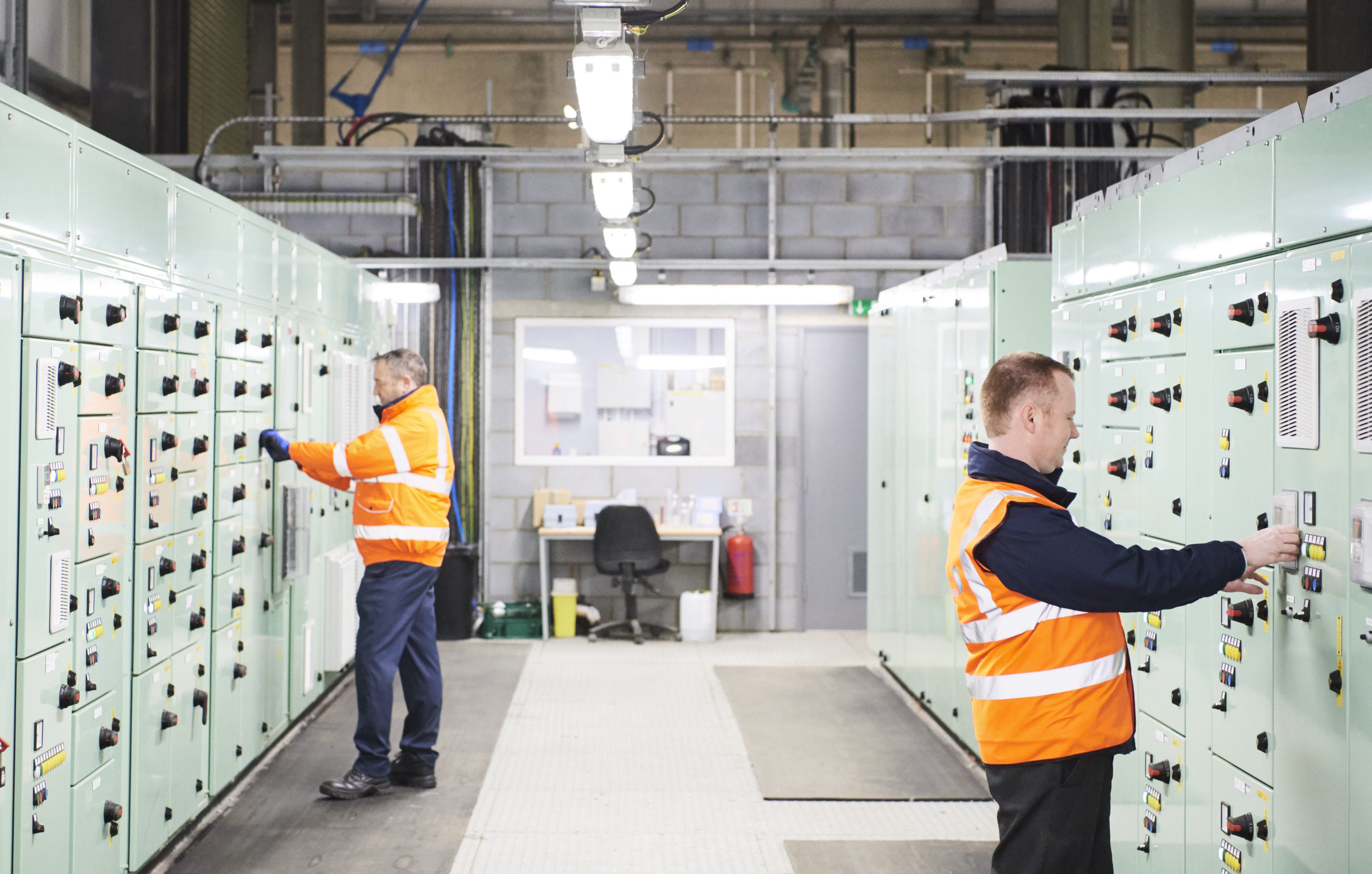 Two males in high vis jackets pressing buttons on machines in water treatment centre