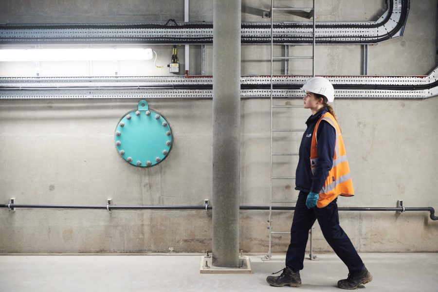 Female apprentice in high vis jacket and hard hat walking through water treatment centre