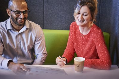 One male and one female colleague sitting on sofa looking at a tablet device