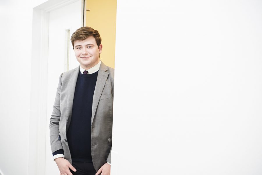 Young man in jacket and tie standing by a door in an office