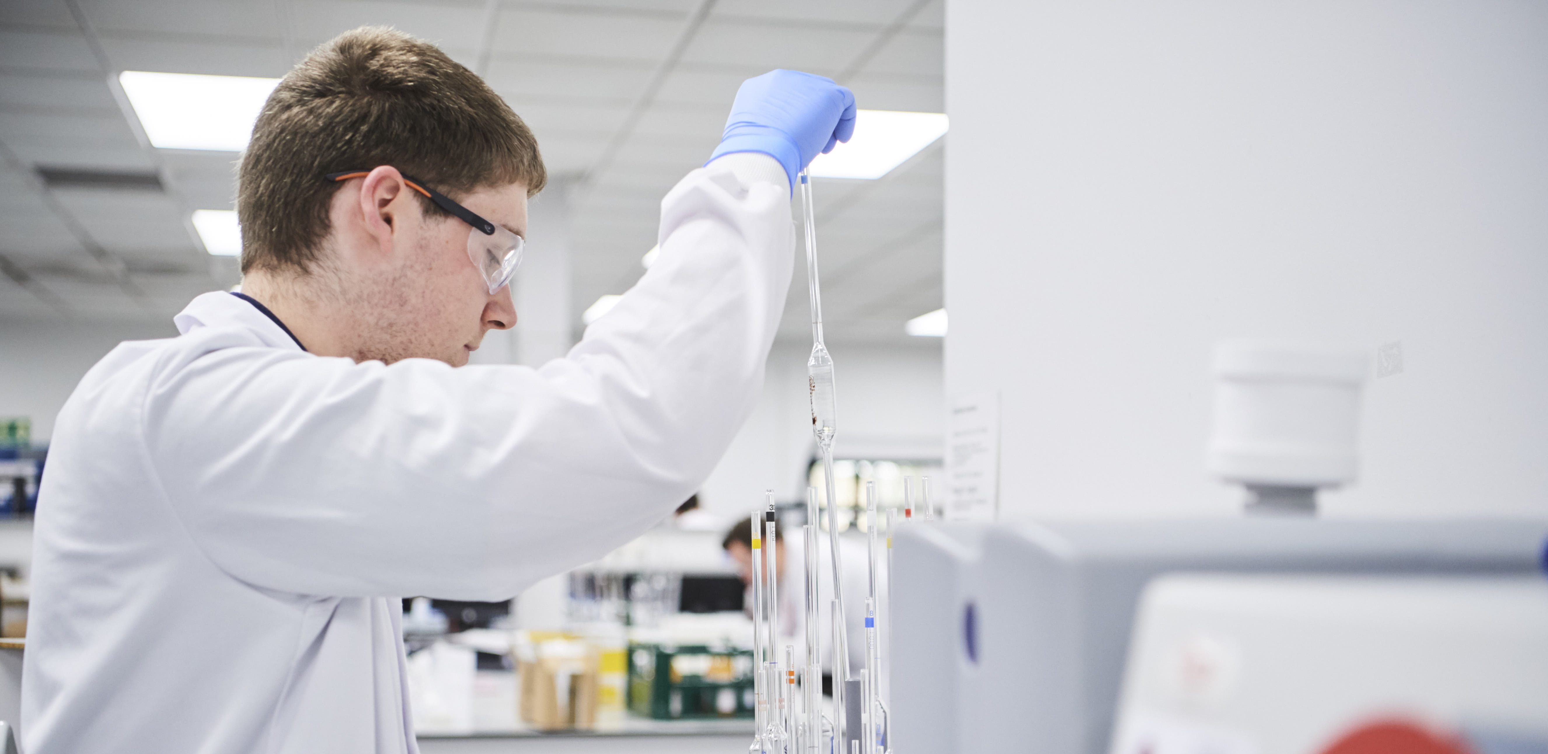 Male in laboratory environment with lab coat and gloves pouring into a test tube