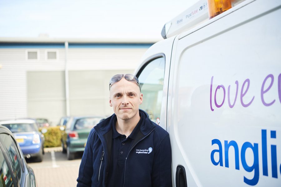 Male Anglian Water employee looking at the camera beside his Anglian Water van