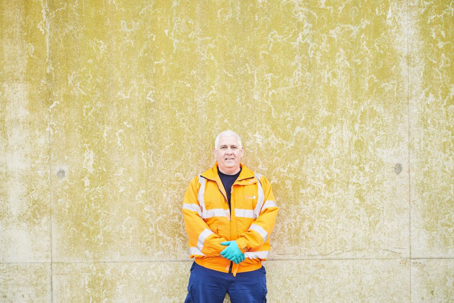 Shot of a man in a high vis coat and hygienic gloves leaning against an old wall at a treatment facility