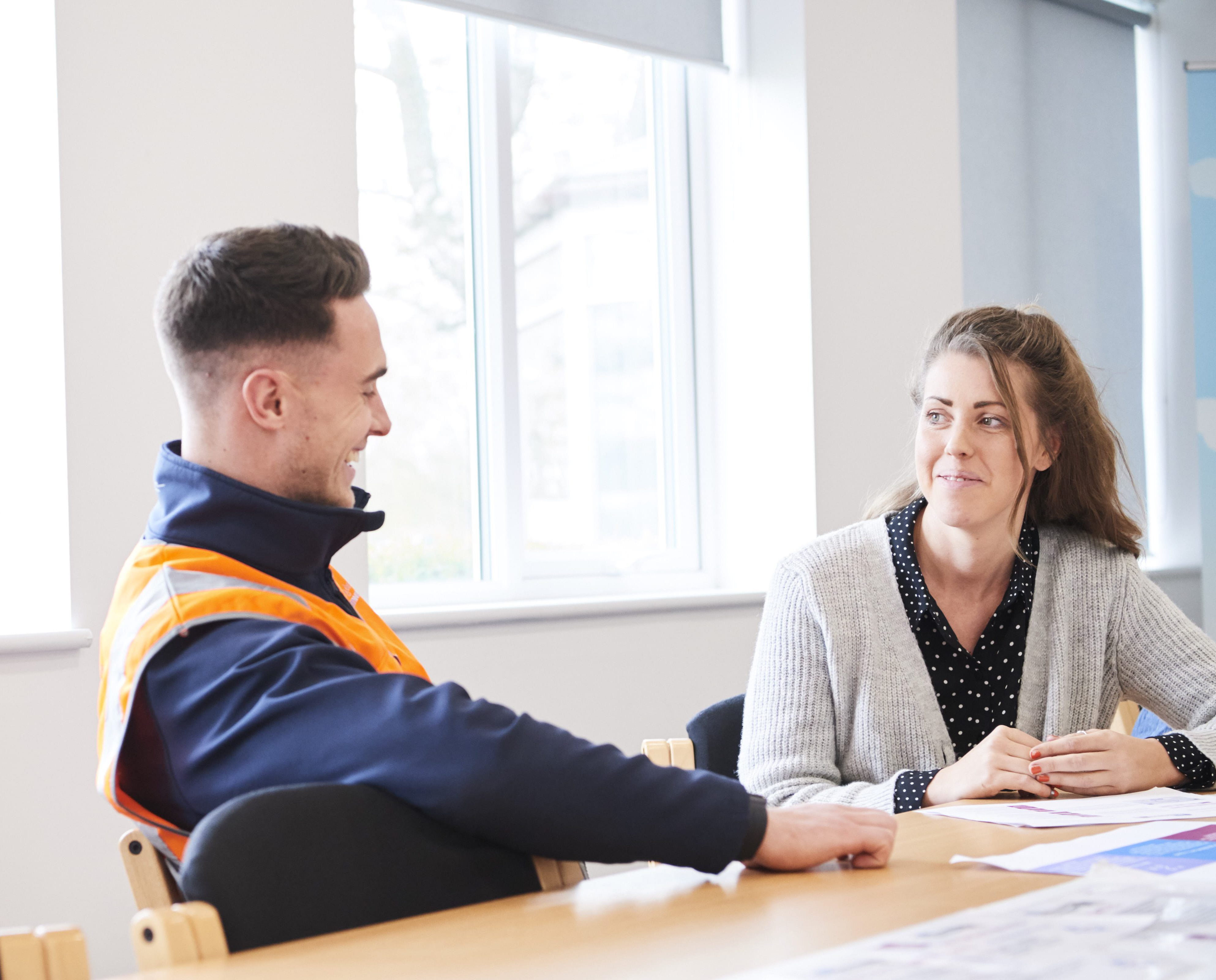 Male in high vis talking to female co-worker at table