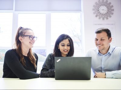 Two female and one male in an office environment looking at a laptop